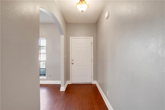 foyer with arched walkways, dark wood-style flooring, and baseboards