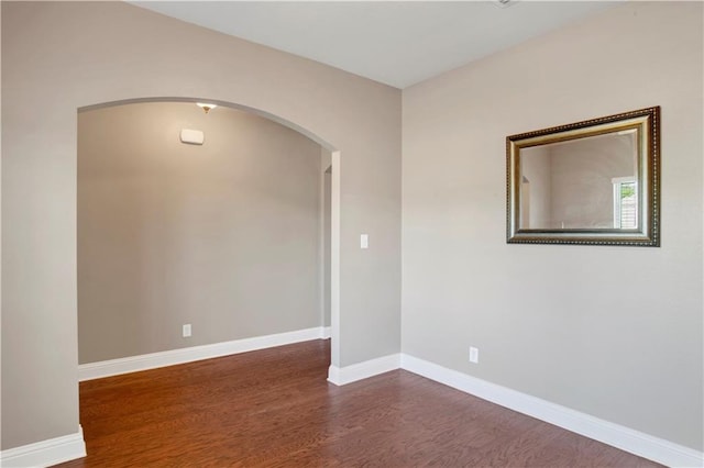 unfurnished room featuring arched walkways, dark wood finished floors, and baseboards