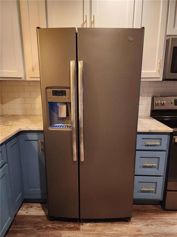 kitchen with decorative backsplash, hardwood / wood-style flooring, white cabinets, and appliances with stainless steel finishes