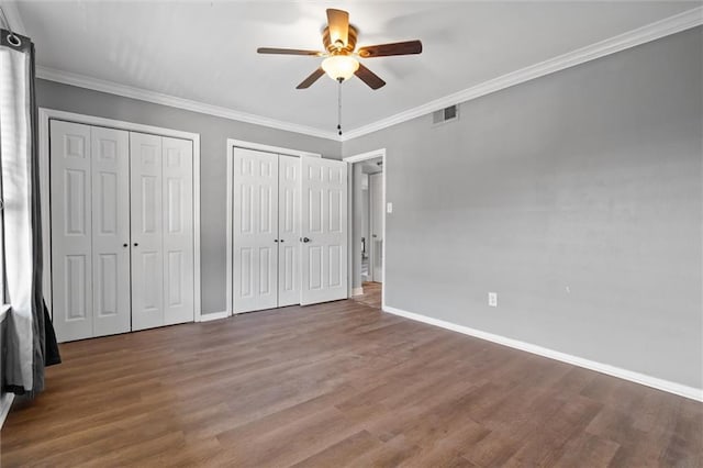 unfurnished bedroom featuring ceiling fan, crown molding, two closets, and hardwood / wood-style flooring