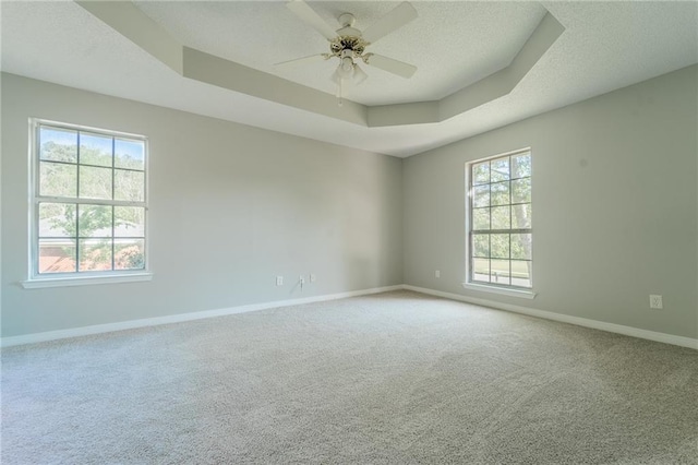 unfurnished room with a raised ceiling, ceiling fan, carpet flooring, and plenty of natural light