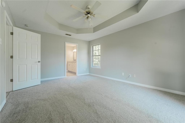 unfurnished bedroom with connected bathroom, ceiling fan, light carpet, and a tray ceiling