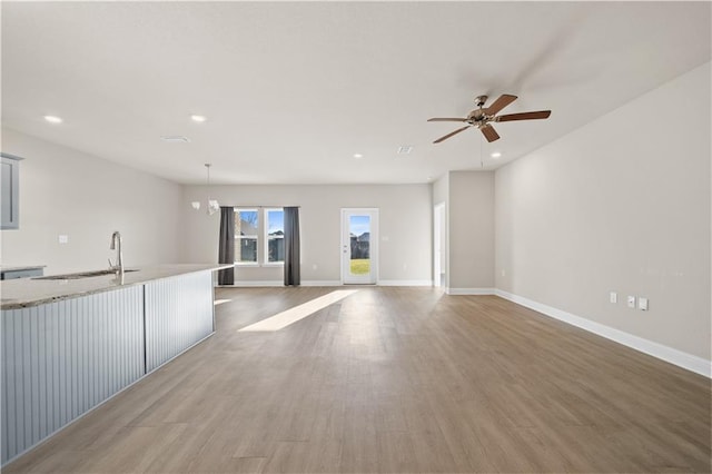 unfurnished living room with wood finished floors, recessed lighting, a sink, and baseboards