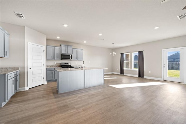 kitchen featuring a kitchen island with sink, gray cabinetry, open floor plan, appliances with stainless steel finishes, and decorative light fixtures