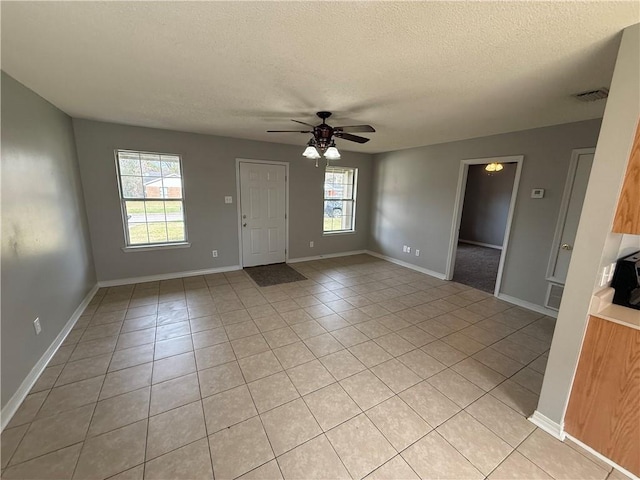 empty room with visible vents, a ceiling fan, a textured ceiling, light tile patterned floors, and baseboards