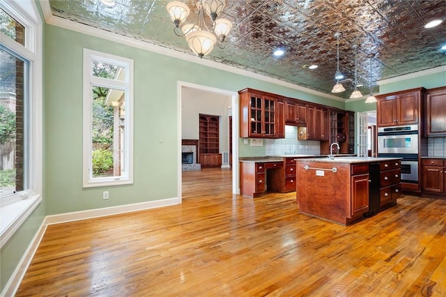 kitchen featuring hanging light fixtures, double oven, crown molding, a kitchen island with sink, and hardwood / wood-style flooring