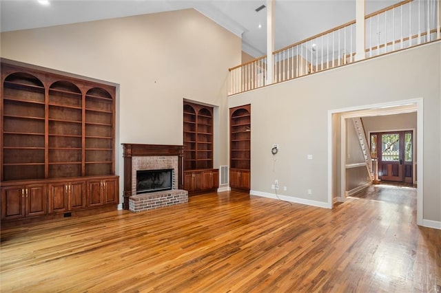 unfurnished living room featuring built in shelves, high vaulted ceiling, light hardwood / wood-style floors, and a brick fireplace