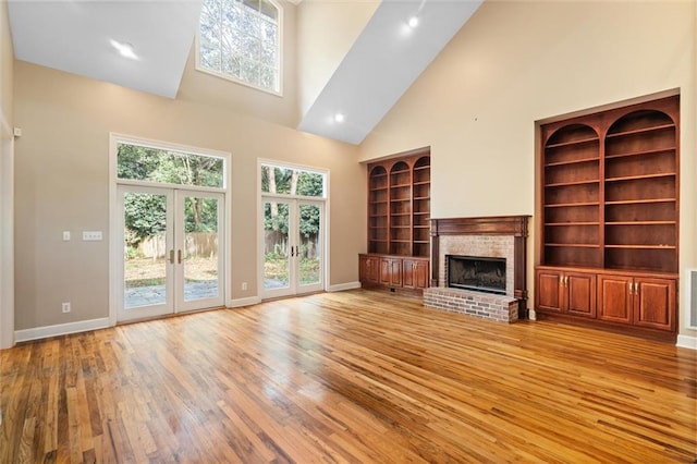 unfurnished living room with a brick fireplace, french doors, high vaulted ceiling, and light hardwood / wood-style flooring