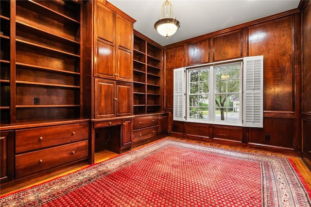 unfurnished office with built in shelves, wood walls, built in desk, and light wood-type flooring