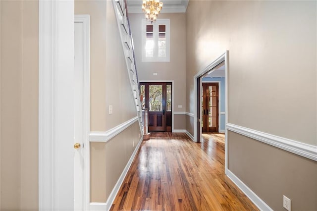 interior space featuring a chandelier, wood-type flooring, a towering ceiling, and crown molding