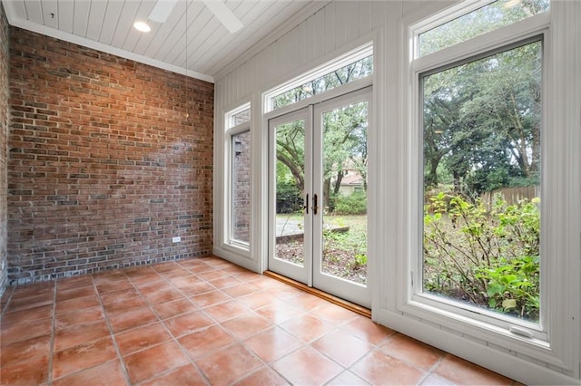 doorway featuring a wealth of natural light, light tile patterned floors, brick wall, and ceiling fan