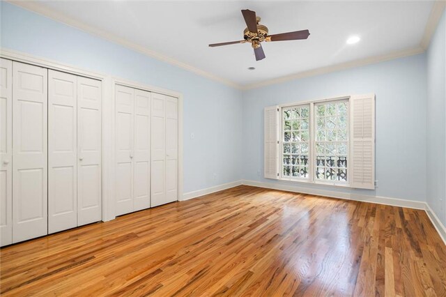 unfurnished bedroom with ceiling fan, light hardwood / wood-style floors, crown molding, and two closets