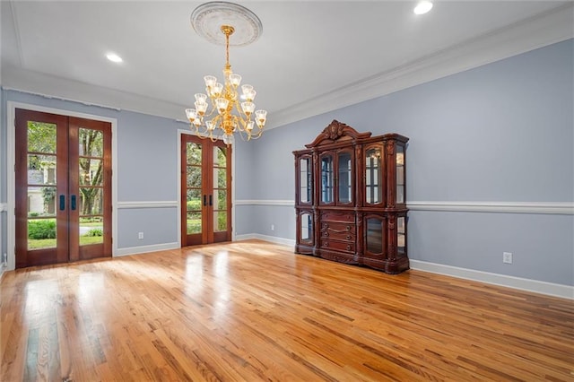 interior space with french doors, light wood-type flooring, an inviting chandelier, and crown molding