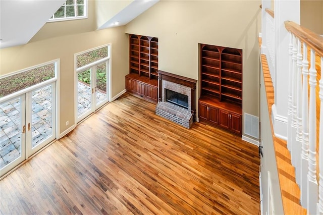 unfurnished living room featuring wood-type flooring, a fireplace, high vaulted ceiling, and french doors