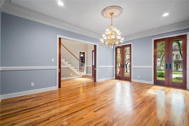 empty room with a chandelier, crown molding, light hardwood / wood-style flooring, and french doors