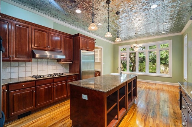 kitchen featuring stainless steel appliances, crown molding, decorative light fixtures, a center island with sink, and light hardwood / wood-style floors