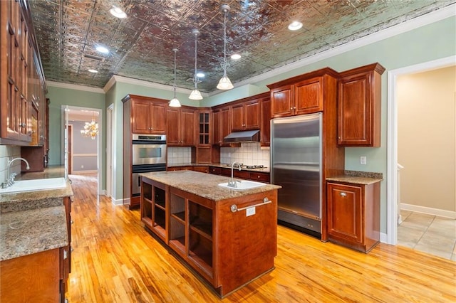 kitchen with sink, light hardwood / wood-style flooring, ornamental molding, an island with sink, and appliances with stainless steel finishes