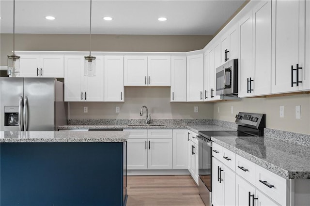 kitchen featuring decorative light fixtures, a sink, light wood-style flooring, stainless steel appliances, and white cabinets
