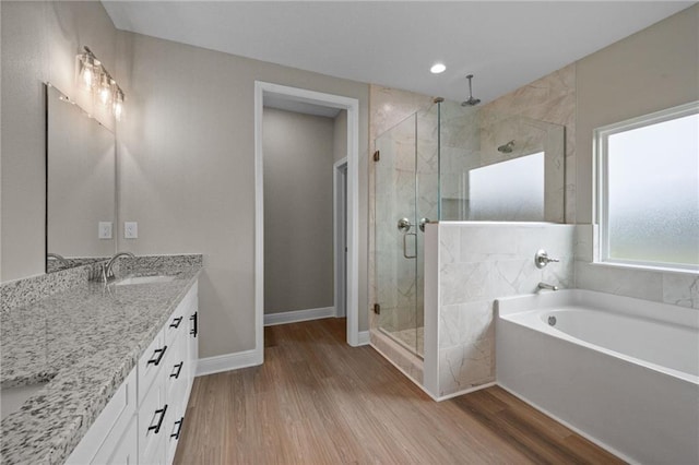full bath with vanity, baseboards, a shower stall, a garden tub, and wood finished floors