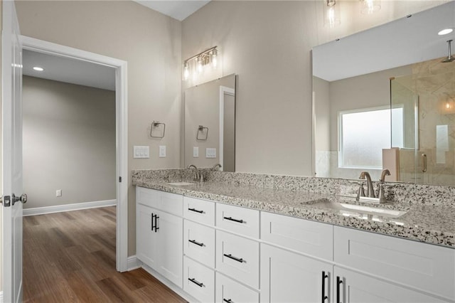 bathroom featuring a stall shower, baseboards, wood finished floors, and a sink