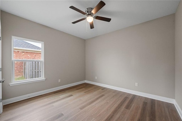empty room featuring a wealth of natural light, wood finished floors, baseboards, and a ceiling fan