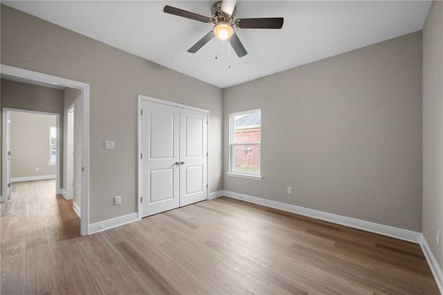 unfurnished bedroom with baseboards, ceiling fan, wood finished floors, and a closet