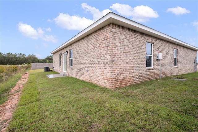 view of side of home featuring central AC unit, a lawn, fence, and brick siding