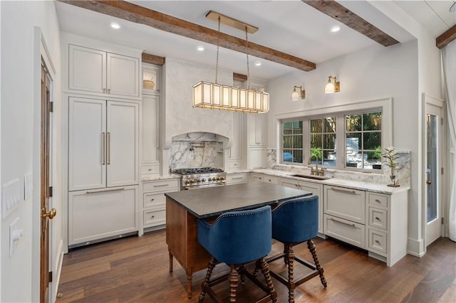 kitchen with a breakfast bar area, beamed ceiling, dark wood-type flooring, sink, and high end range