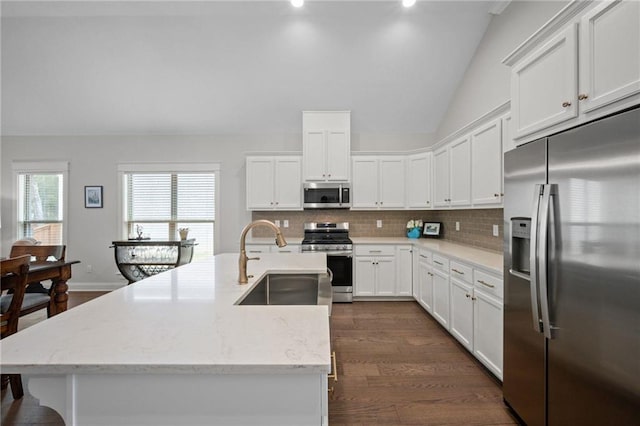 kitchen with decorative backsplash, lofted ceiling, stainless steel appliances, white cabinetry, and a sink