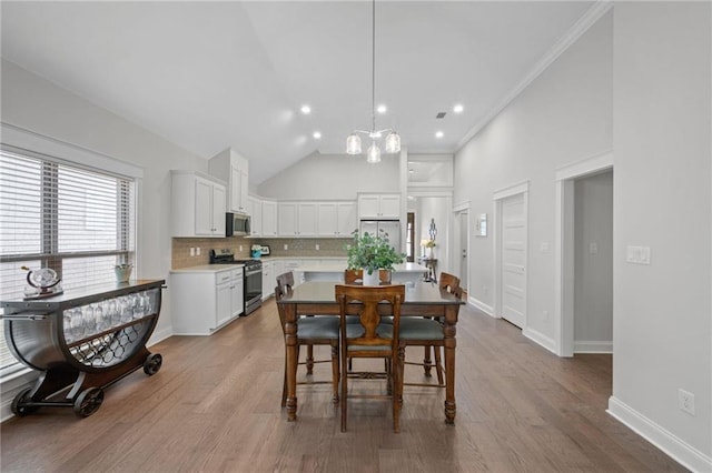 dining area with high vaulted ceiling, ornamental molding, baseboards, and wood finished floors