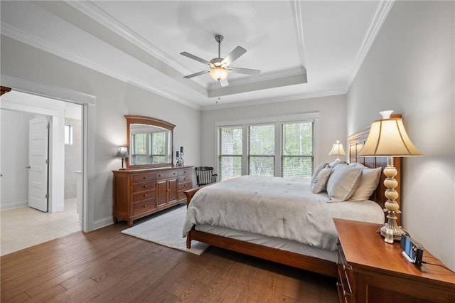 bedroom featuring a tray ceiling, light wood-style flooring, ornamental molding, ceiling fan, and baseboards