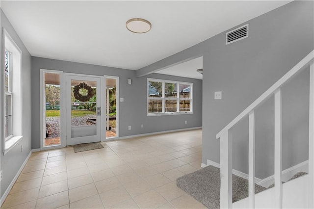 foyer entrance with light tile patterned floors, visible vents, baseboards, and stairs