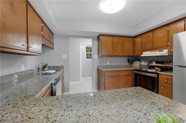 kitchen with brown cabinets, appliances with stainless steel finishes, a sink, under cabinet range hood, and baseboards