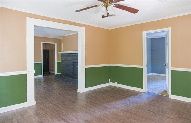 empty room featuring crown molding, a fireplace, dark hardwood / wood-style flooring, and ceiling fan