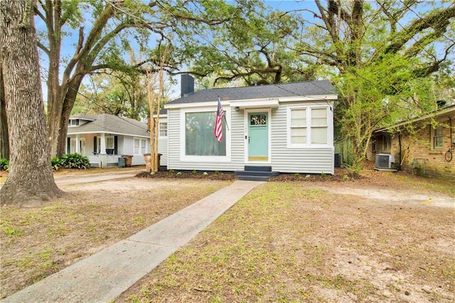 bungalow-style home with entry steps, a chimney, central AC unit, and a front yard