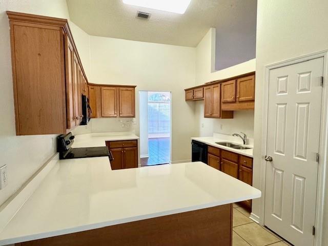 kitchen featuring sink, black dishwasher, stove, light tile patterned floors, and kitchen peninsula