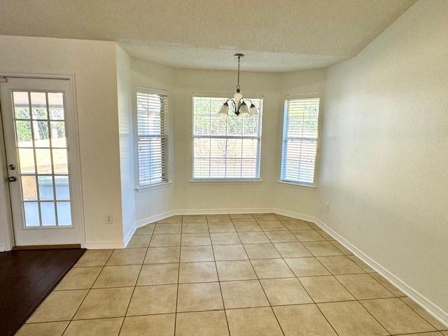 unfurnished dining area with light tile patterned floors, a textured ceiling, and a chandelier