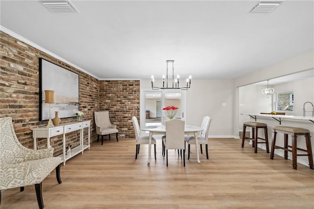 dining room featuring a notable chandelier, brick wall, and light hardwood / wood-style floors