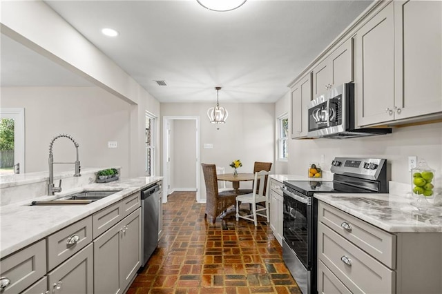 kitchen with stainless steel appliances, light stone countertops, sink, and gray cabinetry