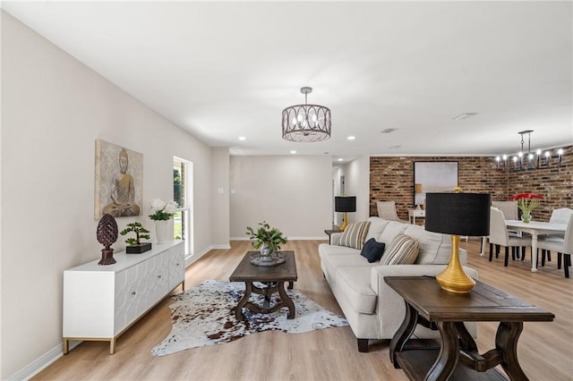 living room featuring brick wall, light wood-type flooring, and an inviting chandelier