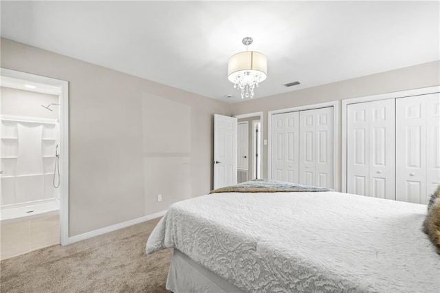 carpeted bedroom featuring ensuite bath, a chandelier, and two closets