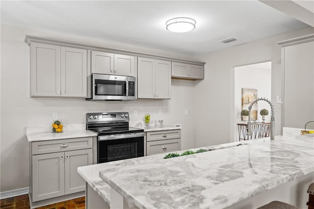 kitchen with gray cabinetry, light stone counters, and appliances with stainless steel finishes