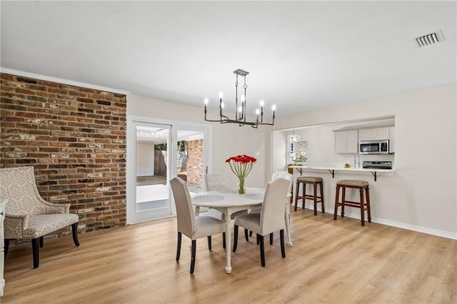 dining area with light hardwood / wood-style flooring, a chandelier, and brick wall