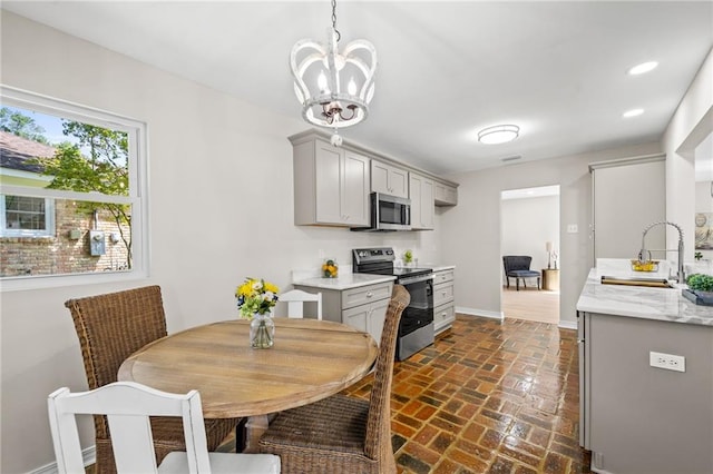 kitchen featuring gray cabinets, pendant lighting, stainless steel appliances, a chandelier, and sink