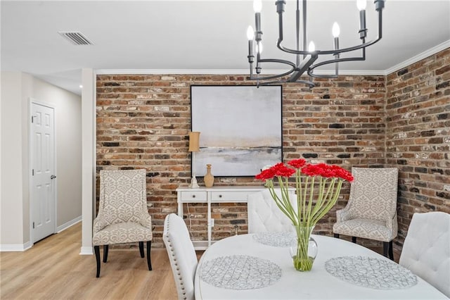 dining space with ornamental molding, brick wall, a chandelier, and light wood-type flooring