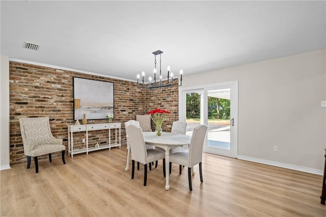 dining area featuring brick wall, light hardwood / wood-style flooring, and a notable chandelier