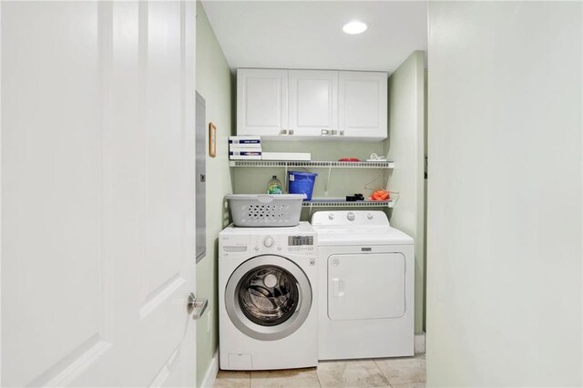 clothes washing area with washing machine and clothes dryer, cabinet space, and light tile patterned floors
