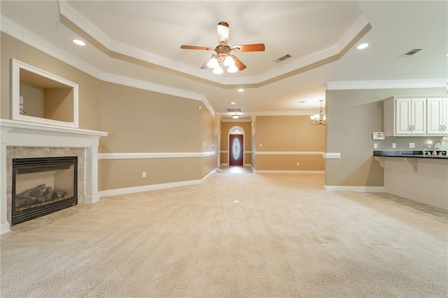 unfurnished living room featuring ornamental molding, a tray ceiling, a tile fireplace, light carpet, and ceiling fan with notable chandelier