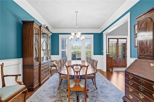 dining space with a chandelier, wainscoting, crown molding, and wood finished floors