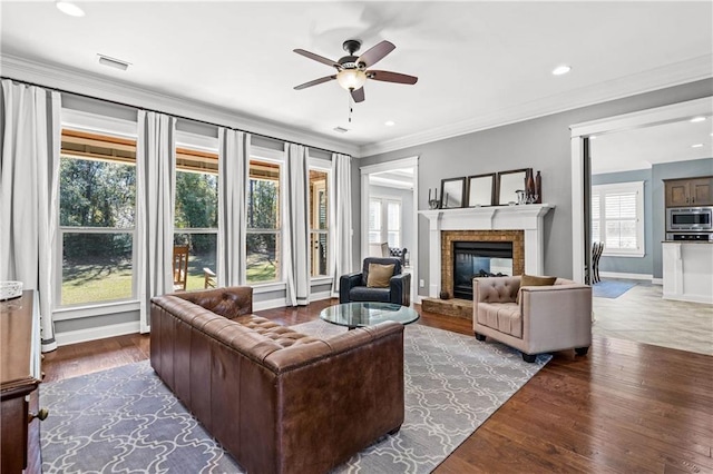 living area featuring recessed lighting, ornamental molding, a glass covered fireplace, wood finished floors, and baseboards